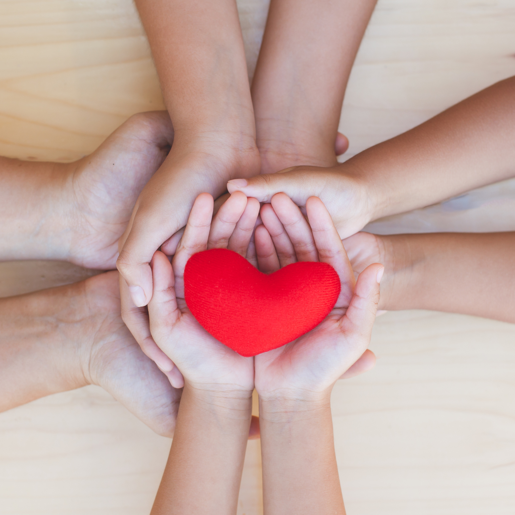 Family and friends stack hands with red heart showing unity, generosity, teamwork and love.